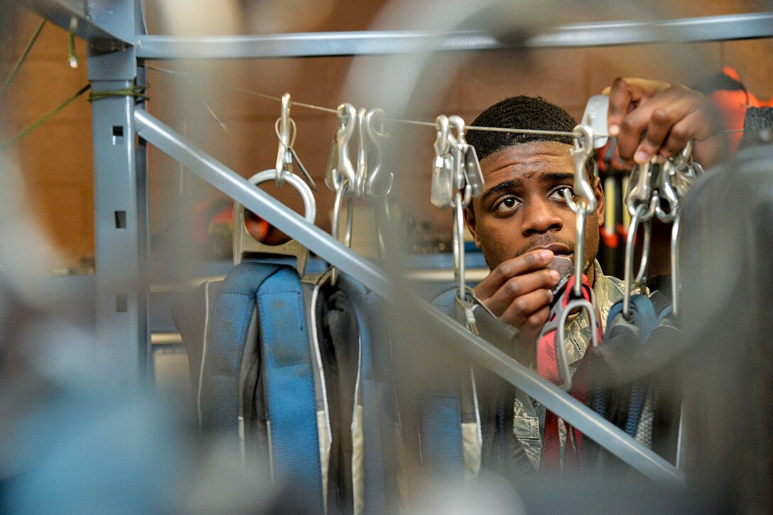 An airman handles harness hanging on a cord on a metal rack.