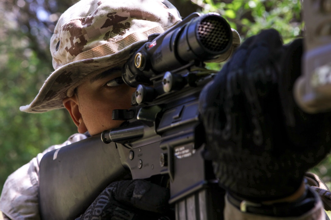 A Marine looks through a rifle scope while aiming the weapon.