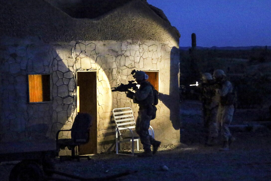 Marines aim their weapons as they approach a building at night.
