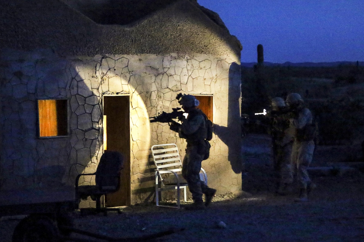 Marines aim their weapons as they approach a building at night.