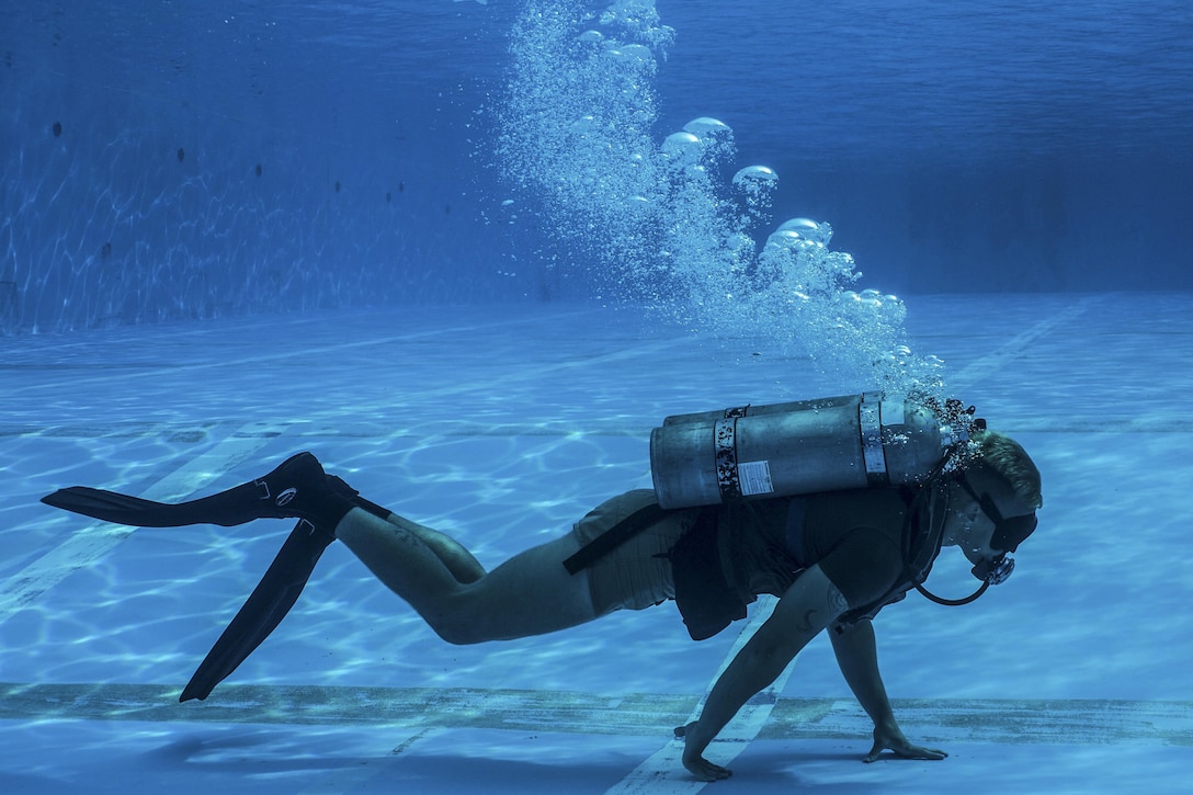 A Marine with breathing gear walks on his hands underwater.