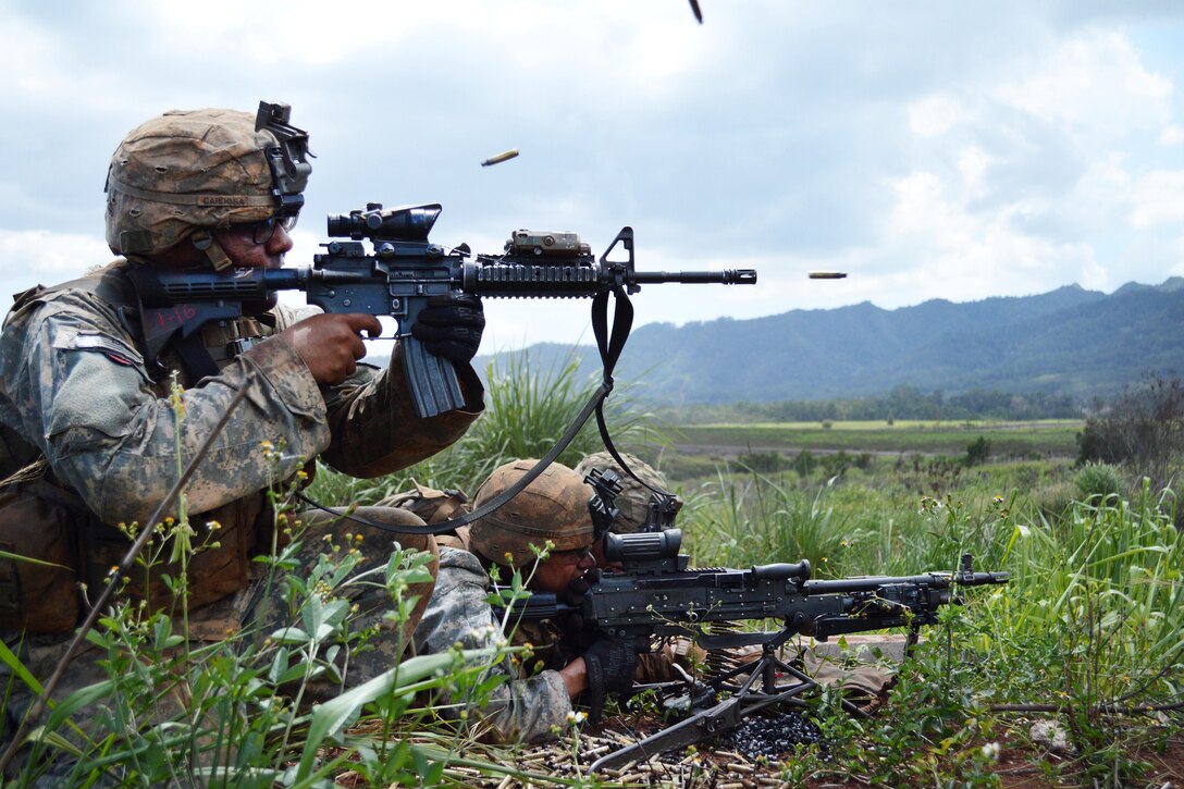 Soldiers fire M4 rifles and machine guns at a target.