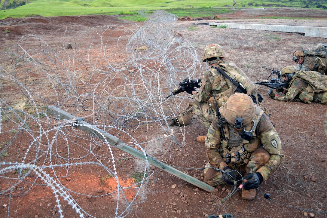 A soldier prepares an improvised bangalore torpedo for detonation at a barbwire obstacle.