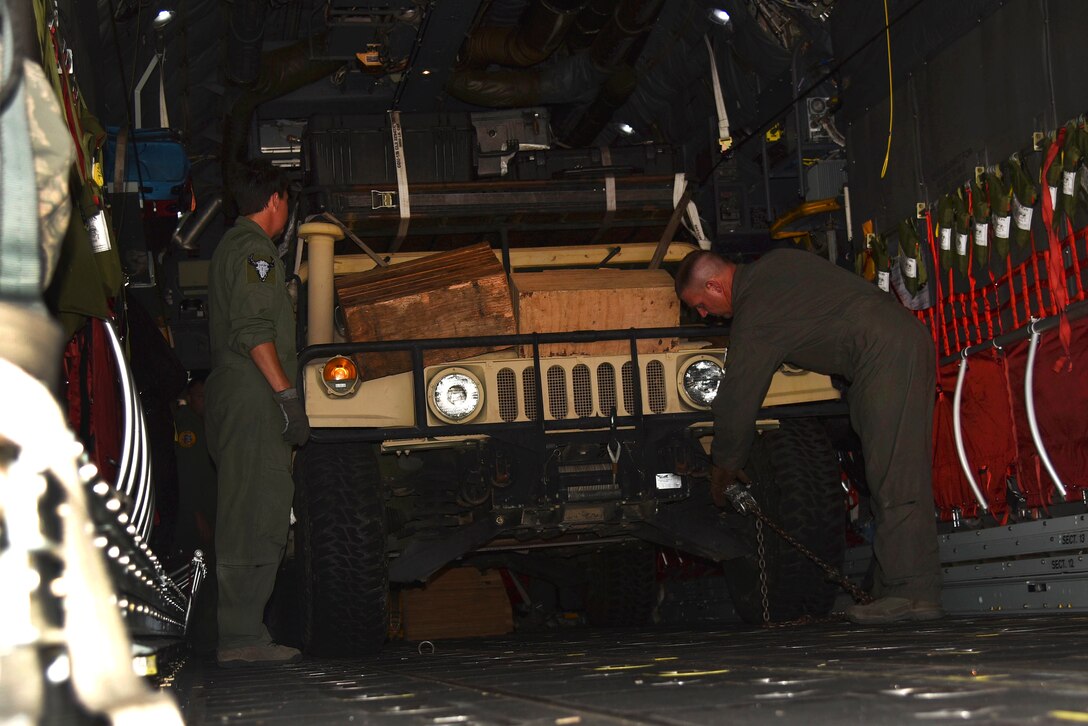 Two airmen remove a military vehicle from an aircraft.