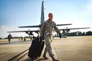 An airman walks with a suitcase behind an aircraft.