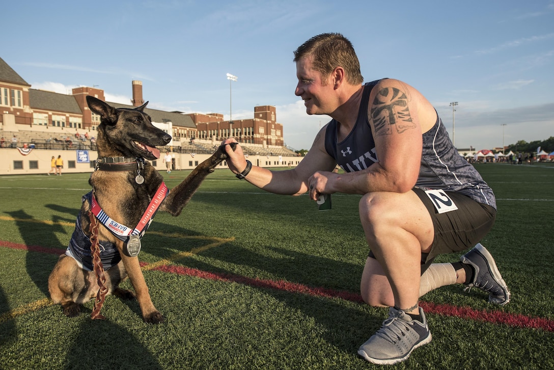 An athlete pauses to shake hands with a dog on a green field.