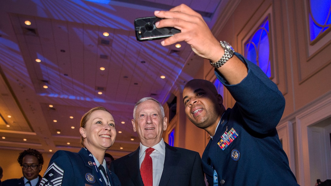 Defense Secretary Jim Mattis poses for photos with two airmen.