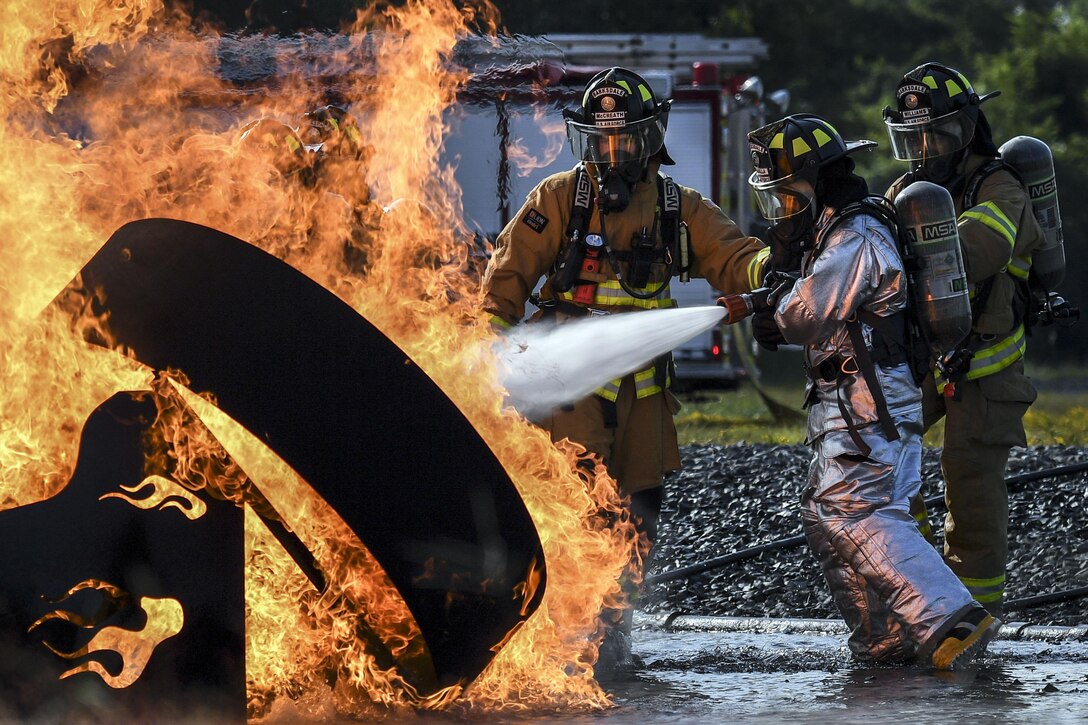 Firefighters train a hose on a fire burning a metal structure.