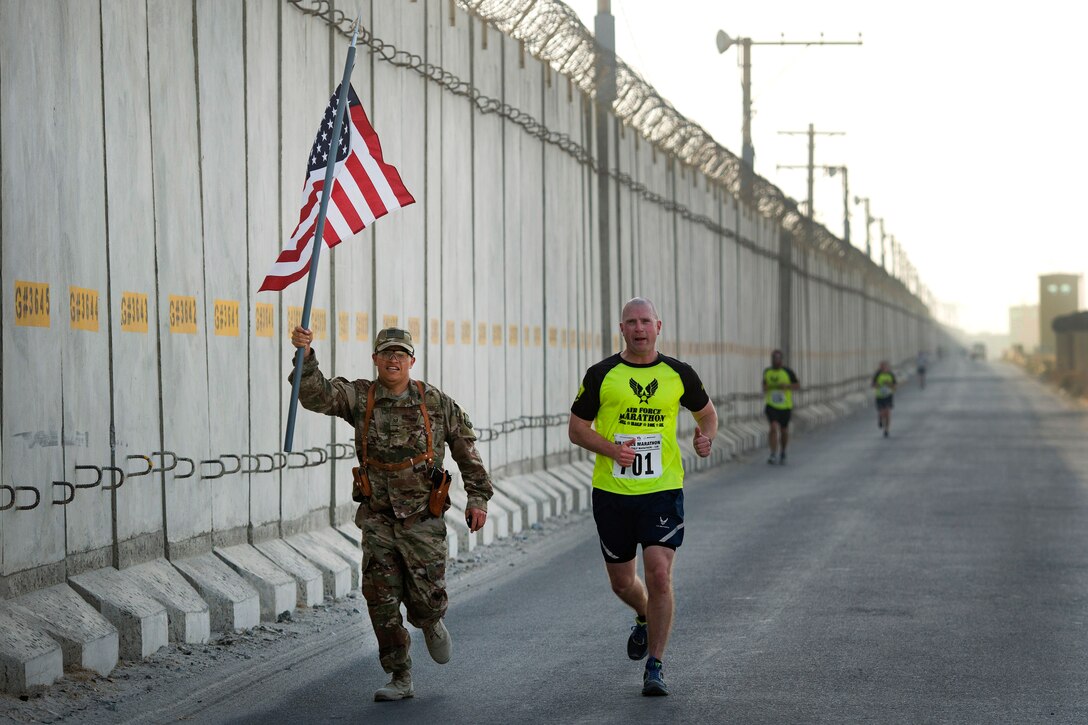 An airman raises and American flag over his head while running.