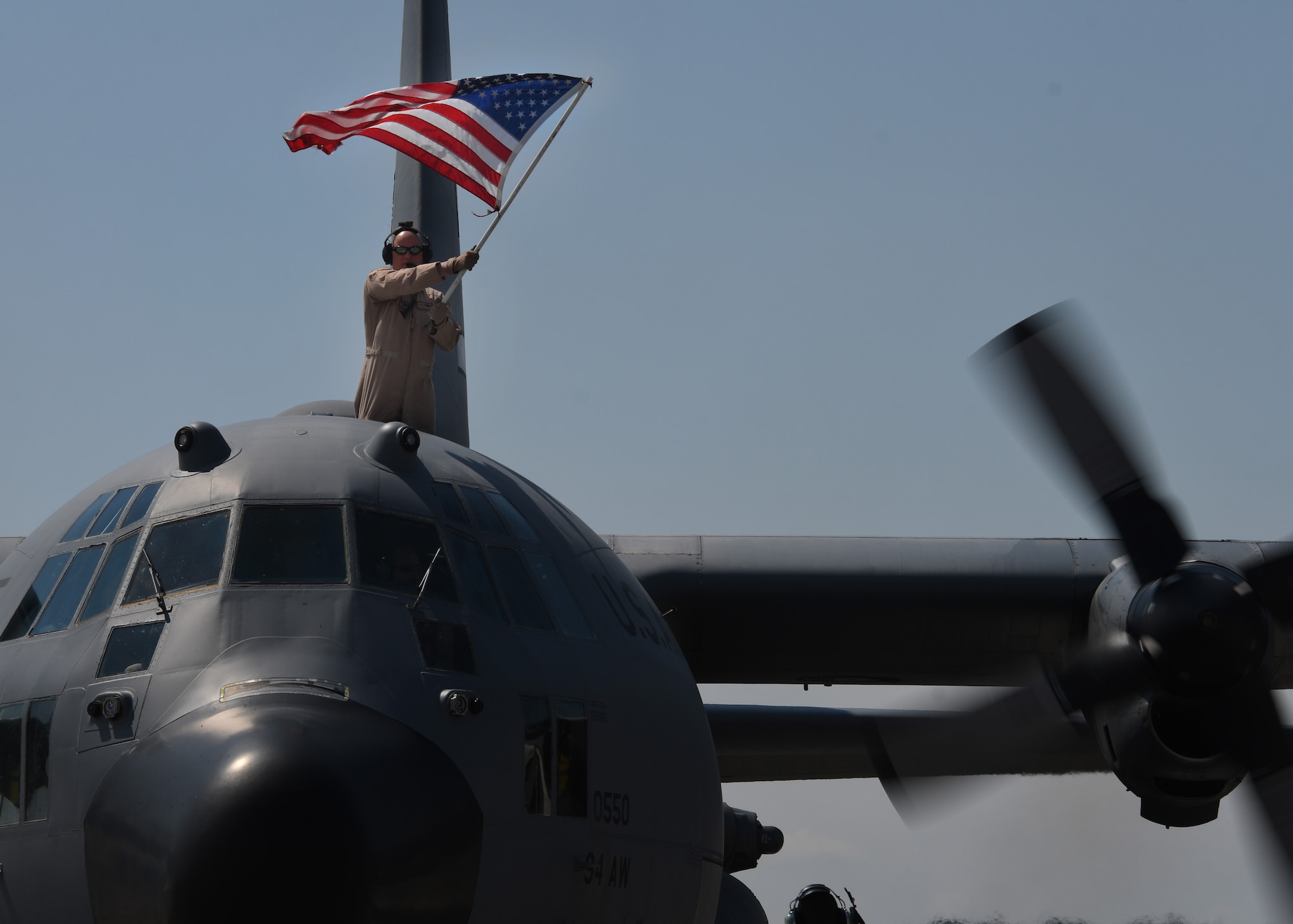 A service member holds an American Flag from the top of a C-130H3 Hercules at Dobbins Air Reserve Base, Ga, Sept. 18, 2017. Five aircraft, along with their aircrews, returned to the 94th Airlift Wing following a deployment to Al Udeid Air Base, Qatar. (U.S. Air Force Photo by Staff Sgt. Miles Wilson)