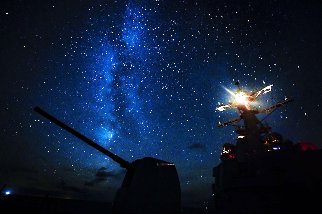 Stars illuminate a dark blue sky that is framing the top of a silhouetted ship.