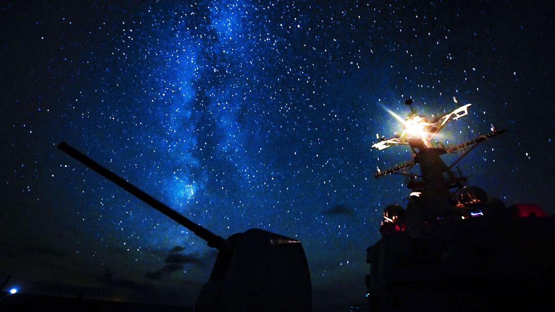 Stars illuminate a dark blue sky that is framing the top of a silhouetted ship.