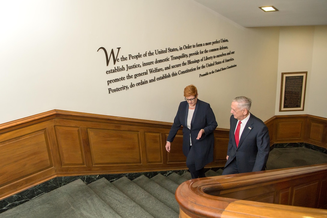 Defense Secretary Jim Mattis walks with the Australian defense minister walk up a flight of steps with writing on the wall.