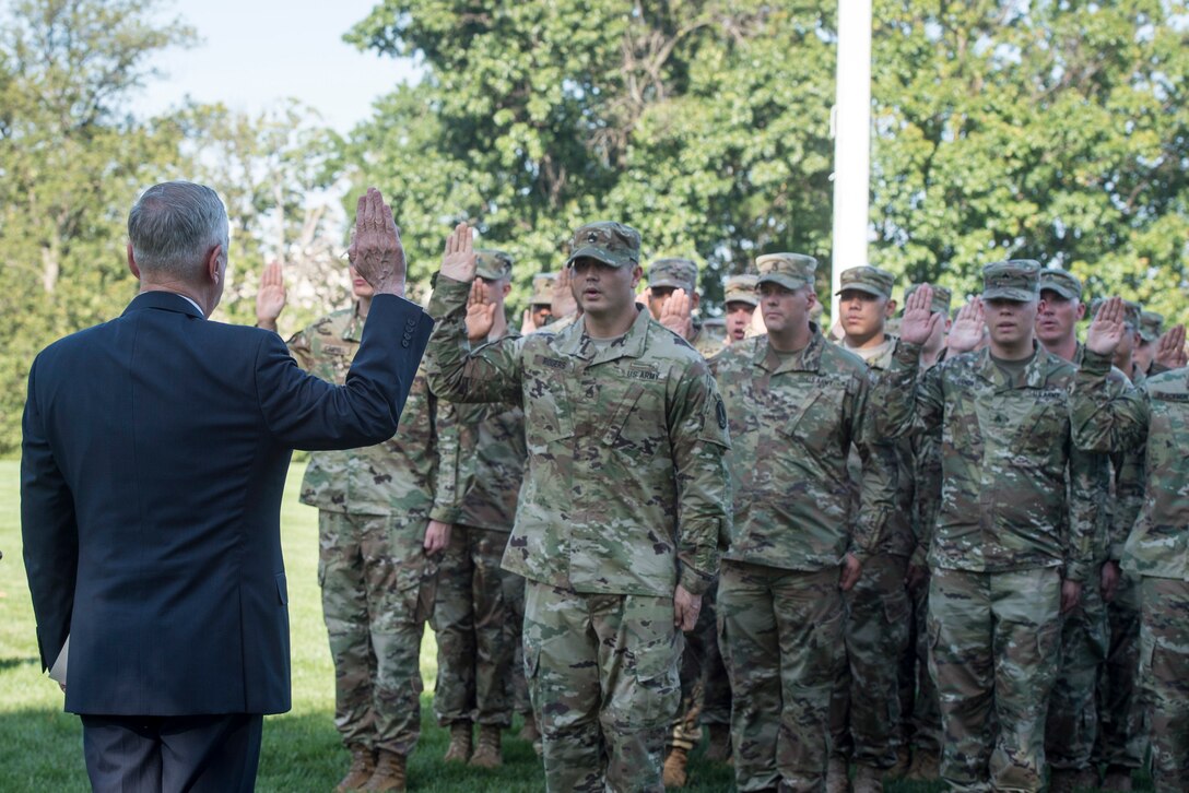 Defense Secretary Jim Mattis stands facing a group of soldiers all with their hands raised.