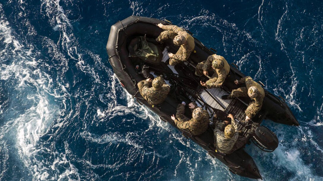 Marines in a rubber boat, seen from above, travel in blue waters.