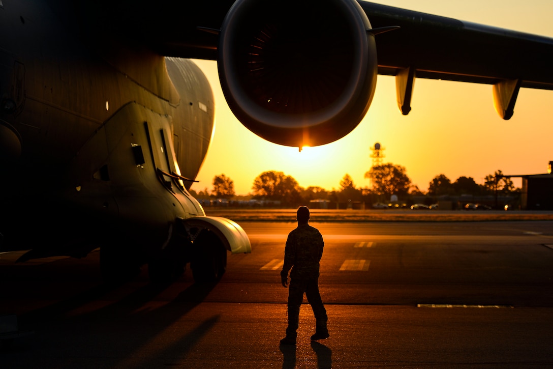 An airman walks around an aircraft at sunset.