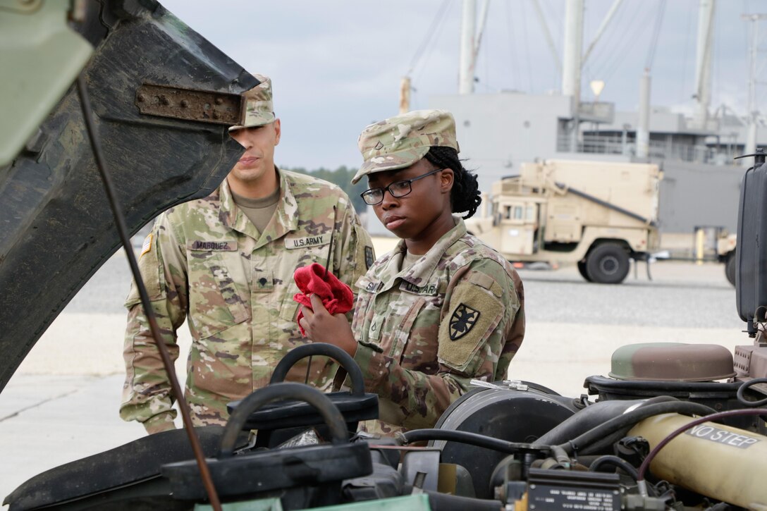 Two soldiers look at a vehicle engine.