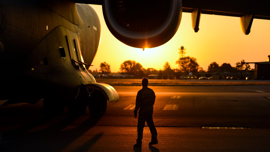 An airman walks around an aircraft at sunset.
