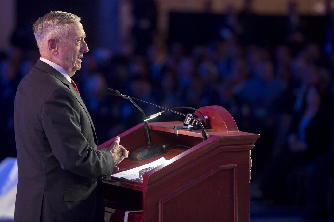 Defense Secretary Jim Mattis speaks from a podium to people in a conference hall.