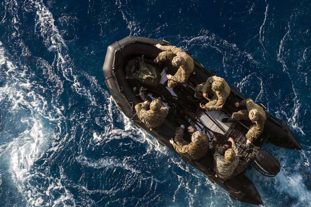 Marines in a rubber boat, seen from overhead, travel in blue waters.