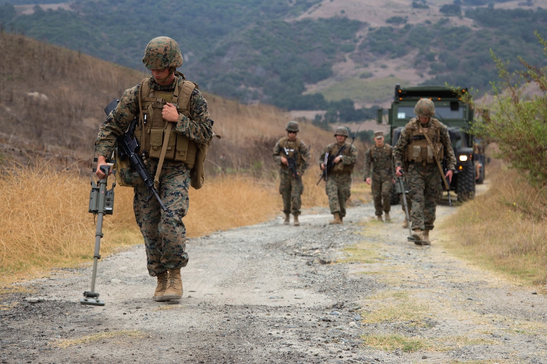 A Marine with a metal detector walks ahead of a group of Marines.