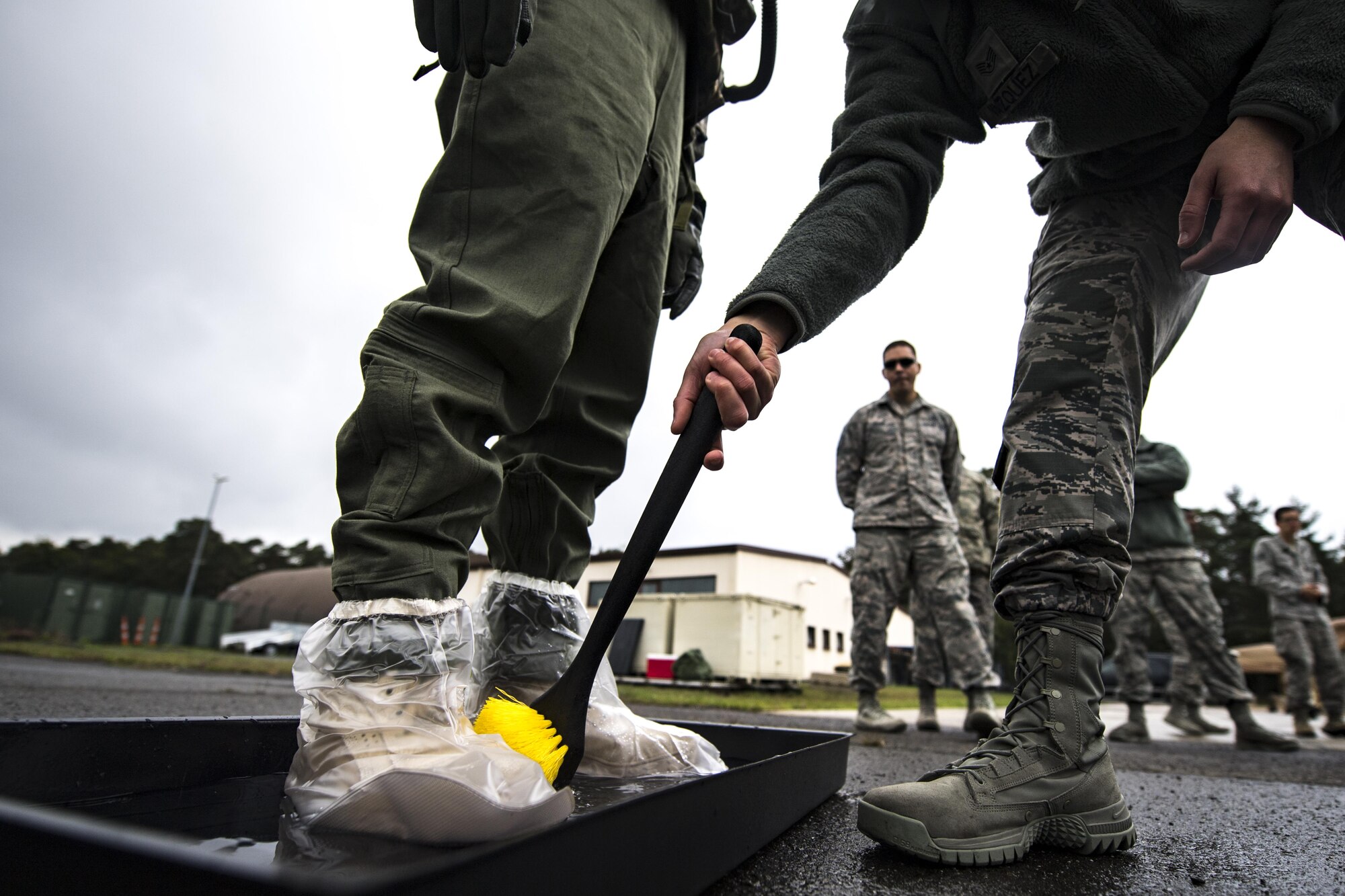 A U.S. Air Force Aircrew Flight Equipment technician decontaminates another AFE technician in a boot wash tray during the Aircrew Contamination Mitigation course on Ramstein Air Base, Germany, Sept. 19, 2017.