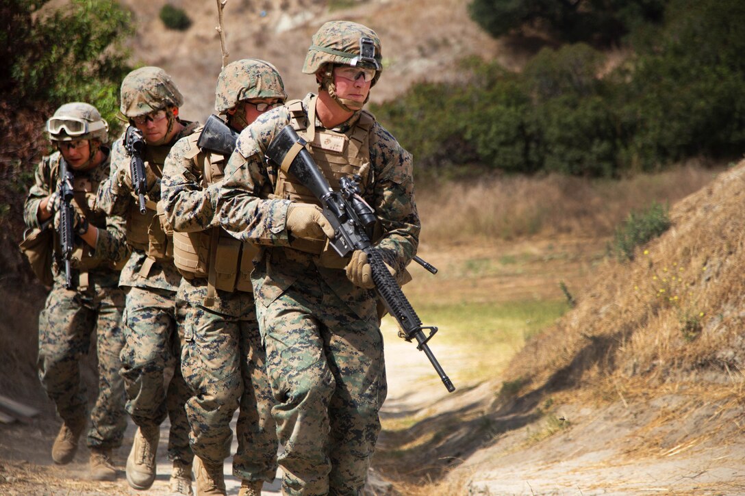 A line of four Marines with weapons walk.