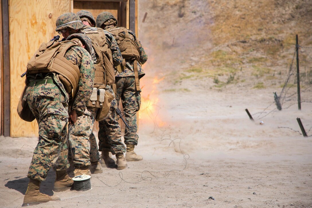 A line of Marines walk toward an explosion.