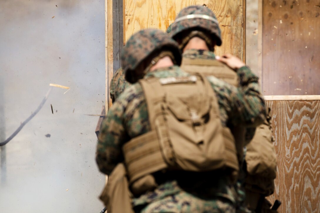 Marines stand behind a wooden wall surrounded by smoke.