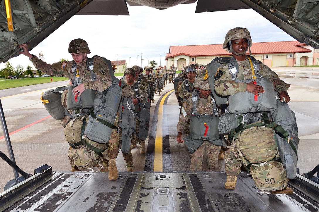 Service members carrying bags walk into an aircraft.
