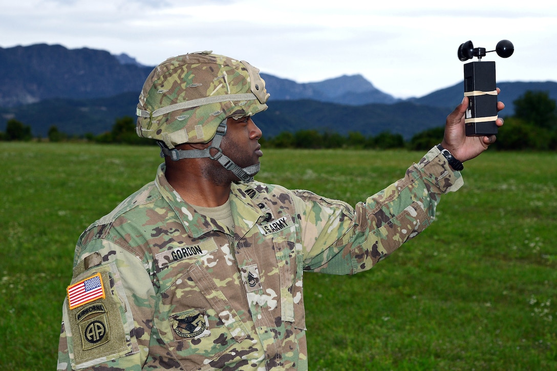 A soldier holds up a device to check wind speed.