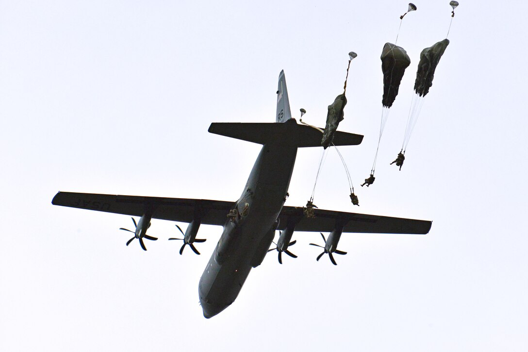 Paratroopers drop from an aircraft in flight.