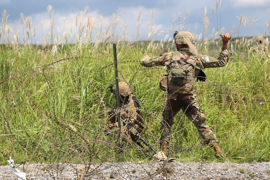 Soldiers prepare to breach a wire obstacle and mark it with a smoke grenade during a live-fire training.