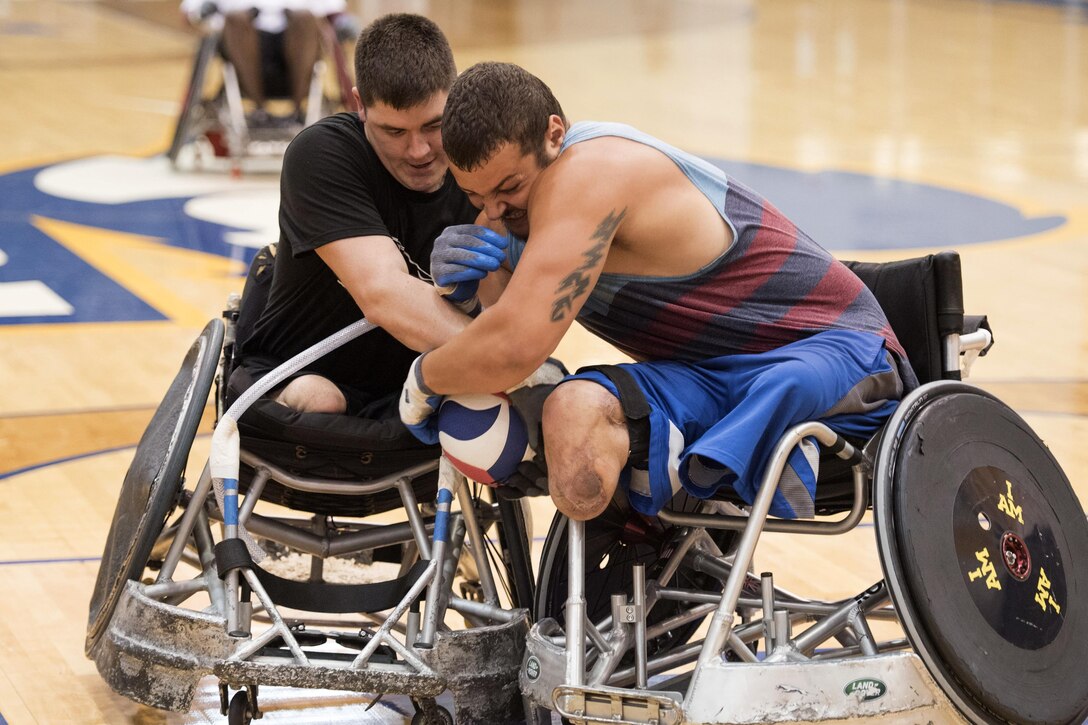 Two people in wheel chairs hold onto a rugby ball.
