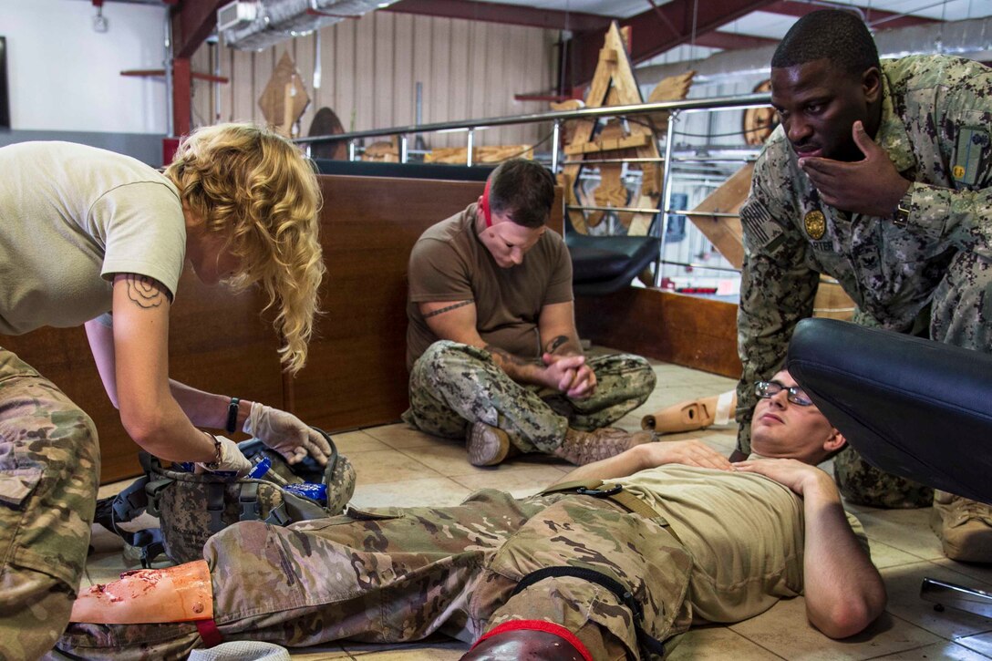 A service member sits and another lays on the ground as an airmen digs though a bad.