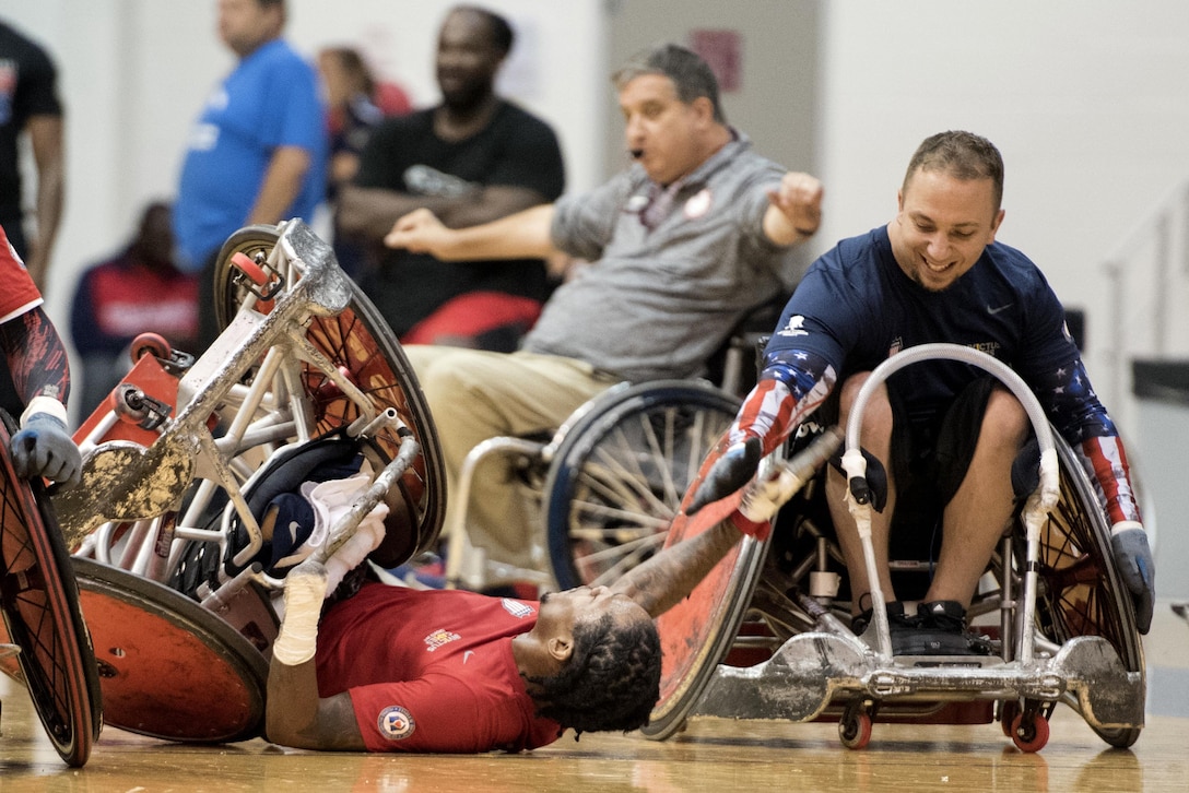 A rugby player in a wheelchair, who fell on the ground, gets a high-five from another player in a wheelchair.