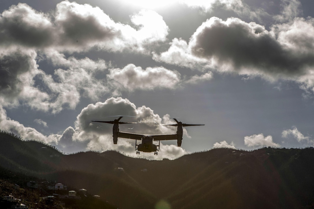 A tiltrotor aircraft flies in a mountainous area.