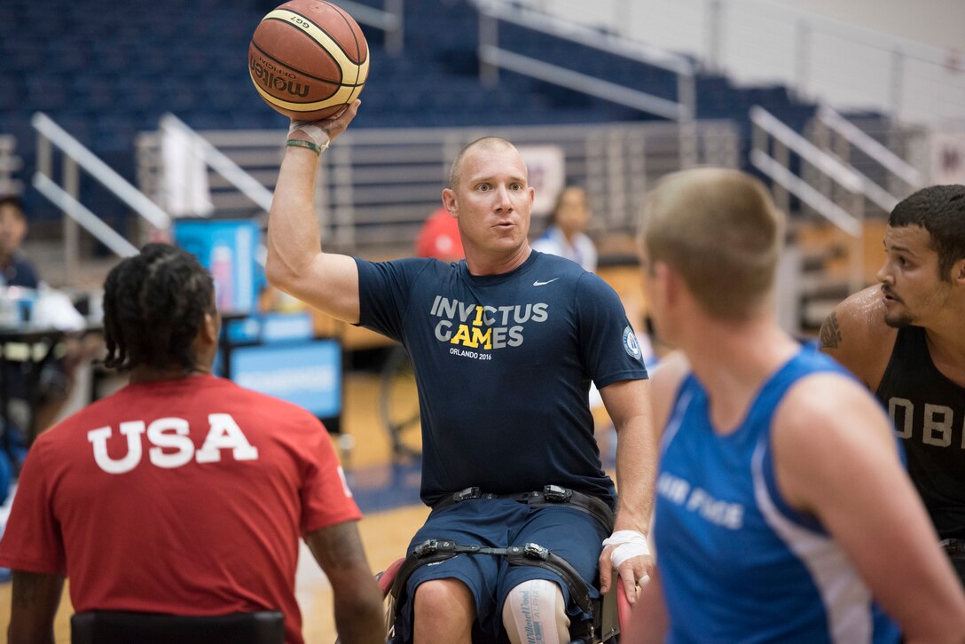 An airman in a wheelchair holds up a basketball while surrounded by three others.