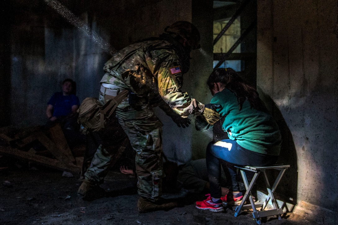 A soldier carefully holds the arm of a role player who appears to be in distress.