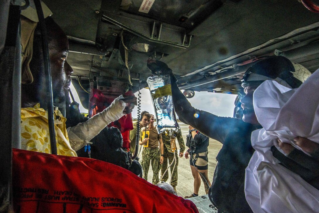 A first responder hangs an IV bag near a patient sitting inside a helicopter.