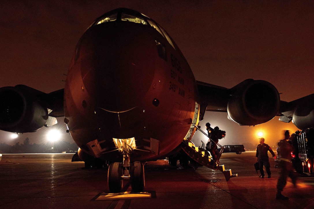 Personnel board an aircraft on a dark flightline.