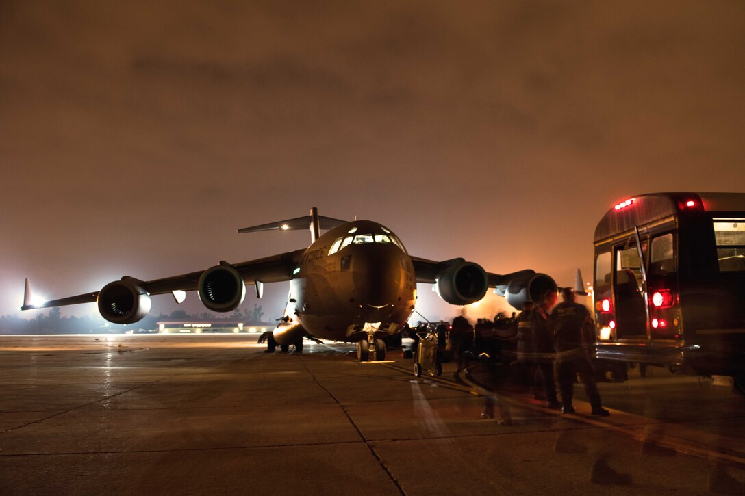 Disaster team members prepare their gear before boarding a C-17 Globemaster III aircraft at night.