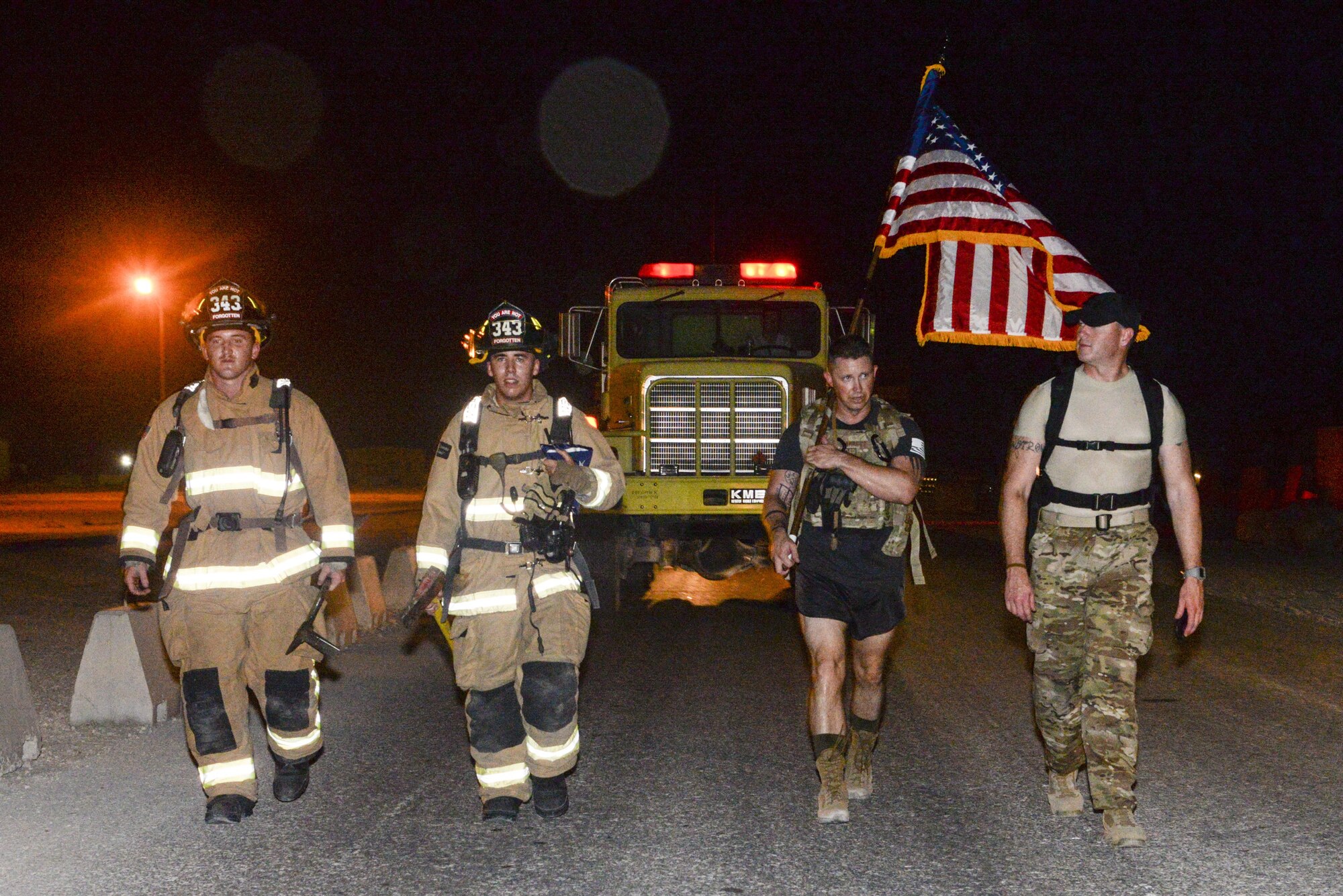 U.S. Air Force Senior Airmen, Cayden Saurbek, left, and John Hodgkind, left center, firefighters assigned to the 379th Expeditionary Civil Engineering Squadron, join Master Sgt. Jason Garrett, holding the flag, security forces member and Capt. Roy Blackledge, right, operations support officer assigned to the 379th Expeditionary Security Forces Squadron, to participate in an evening 9/11 memorial walk at Al Udeid Air Base, Qatar, Sept. 11, 2017.