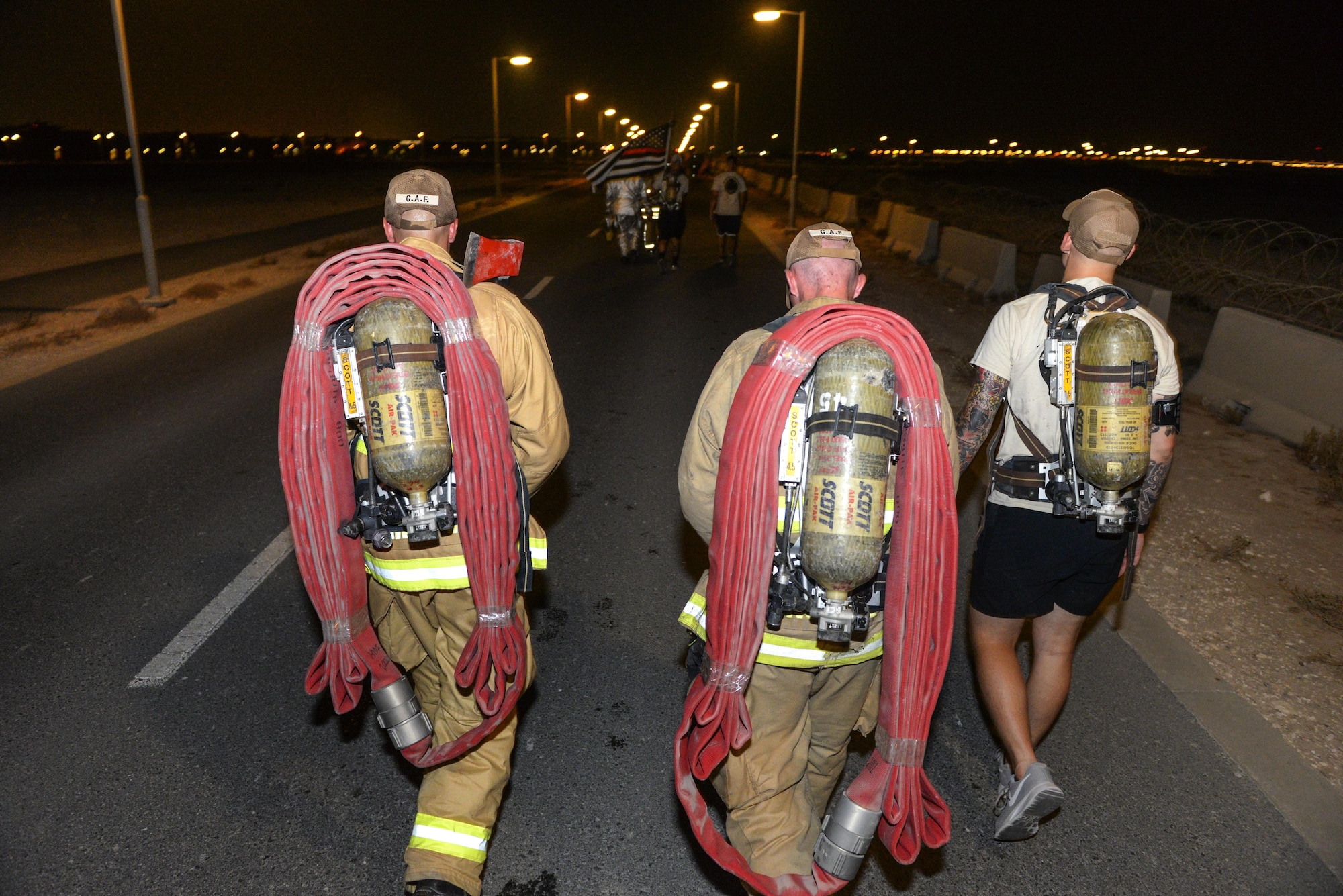 U.S. Air Force firefighters assigned to the 379th Expeditionary Civil Engineering Squadron carry fire hoses and wear self-contained breathing apparatus as they participate in an evening 9/11 memorial walk at Al Udeid Air Base, Qatar, Sept. 11, 2017.