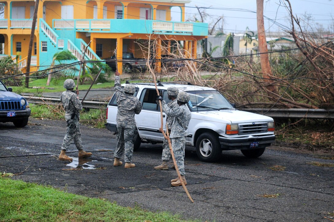 Guardsmen prop up electrical power lines to let vehicles pass on the Melvin Evans highway.