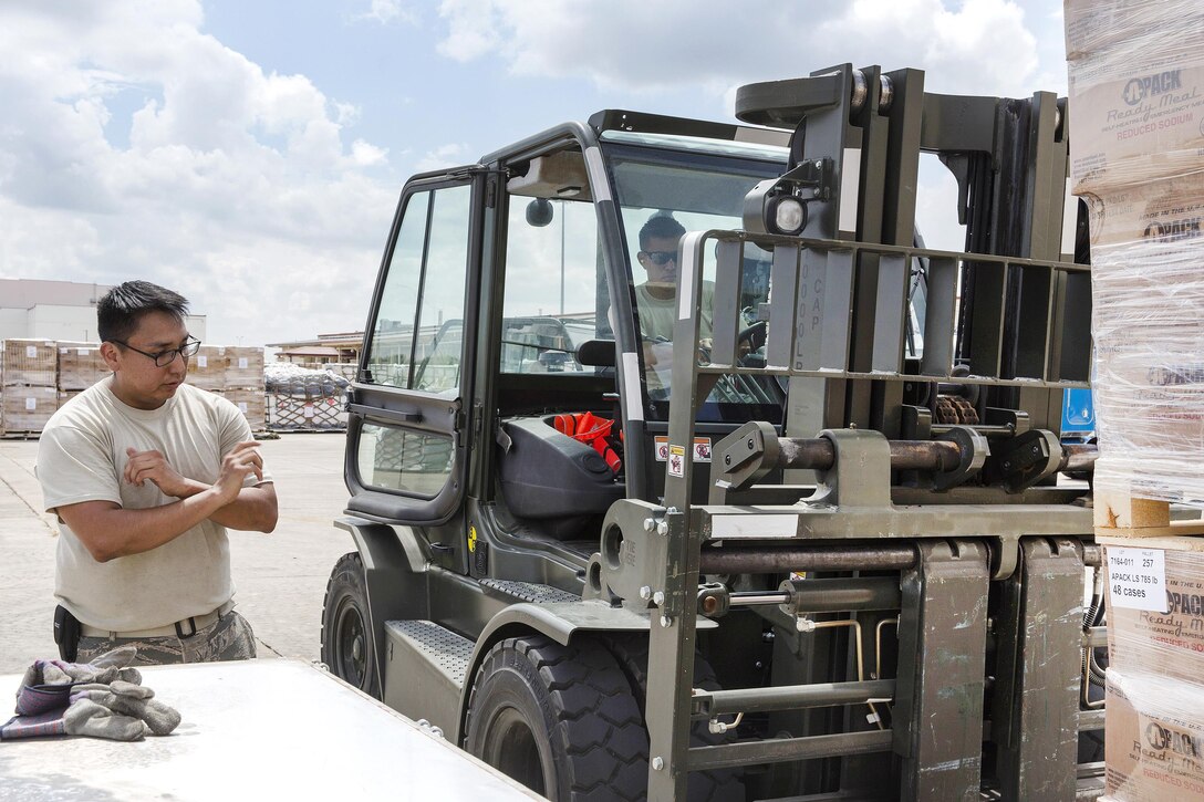 An airman guides another airman operating a forklift moving pallets of water and supplies for transport.
