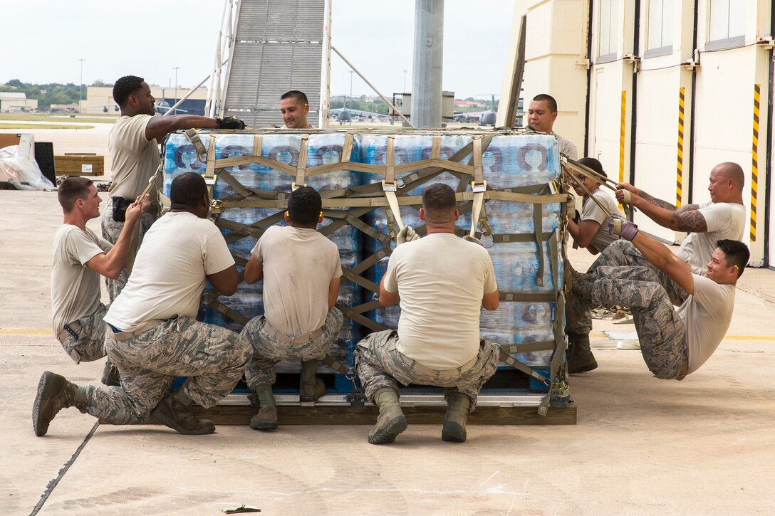 Airmen pull and tighten cargo straps around a large pallet of water and supplies for transport.