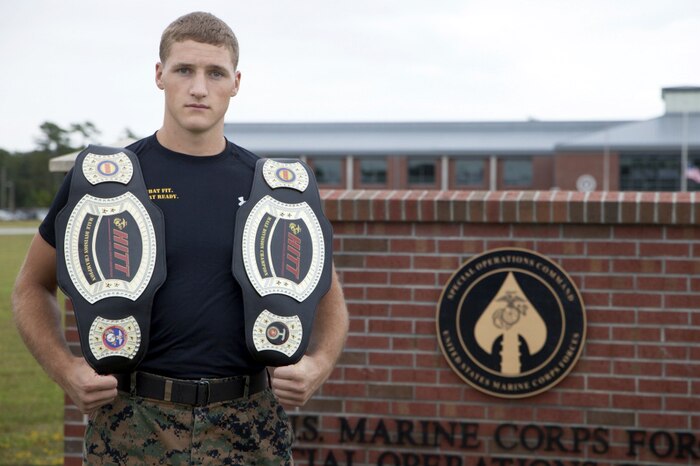 A Marine holds two champion belts on his shoulders and poses for the camera.