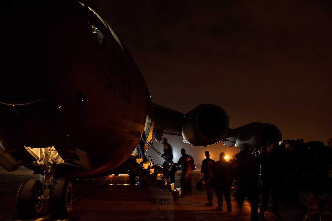 A line of people walk up a flight of steps onto an aircraft in the dark.