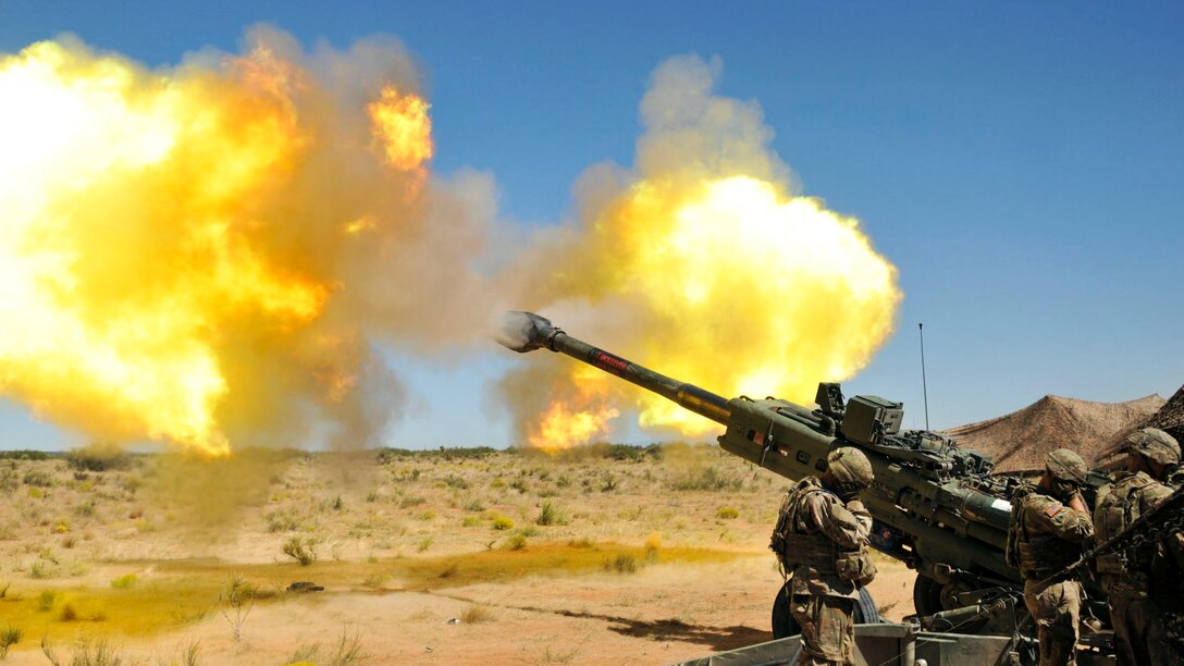 Soldiers cover their ears as a howitzer fires.